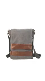 Morral versátil de tela canvas gris con detalles en cuero sintético marrón. Cuenta con tapa frontal con broches magnéticos, bolsillo tipo guantera bajo la tapa, división interna desmontable con velcro y correa larga regulable.