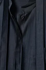 Camisa de corte holgado confeccionada en mezcla de lyocell con acabado satinado. Presenta cuello redondo con lazadas integradas, cierre frontal con botones ocultos bajo solapa, bolsillos de plastrón en el frente y mangas largas con puños anchos. El bajo es asimétrico y redondeado.