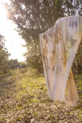 Pañuelo rectangular de tela fina color crema con estampado artesanal de hojas y flores en tonos amarillos y marrones.