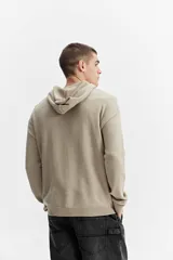 Campera de tejido de punto color beige con capucha, cierre frontal y bolsillos delanteros, de corte oversize y hombros caídos.