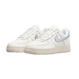 Championes Nike Air Force 1 de corte bajo, con cuerpo de cuero blanco, suela de goma color crema y detalles en tono lila metalizado en el swoosh lateral y el talón.