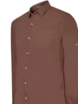 Camisa manga larga color marrón, confeccionada en popelina de algodón orgánico. Tiene cuello italiano, calce regular, bolsillo en el pecho con logo bordado y mangas ajustables con botón.