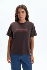 Remera de manga corta color marrón oscuro con estampado frontal que dice "New York City Manhattan 1993" en color rosado.