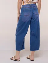 Jean wide leg cropped de tiro medio-alto, confeccionado en denim azul intermedio con efecto degradé y costuras en tono camel. Presenta cinco bolsillos, cierre frontal con botón y cierre, nervaduras decorativas en la zona de las rodillas y ruedo desflecado.