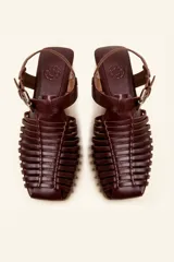 Sandalia de cuero negro estilo huarache, con puntera cerrada mediante tiras finas entretejidas a mano, tira ajustable al tobillo con hebilla metálica y suela plana con taco de 1 cm.