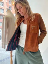 Campera de algodón con delantera de gamuza color tostado, cuello redondo, cierre frontal, bolsillos laterales y bolsillo superior con cierre. Forrería interna con diseño a rayas multicolor.