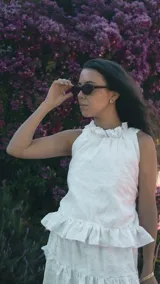 Top halter de broderie blanco con sutil brillo plateado, presenta cuello alto con volados y ruedo con volado amplio. Diseño sin mangas, femenino y ligero.