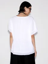 Blusa blanca de lino con cuello redondo y mangas cortas con terminación desflecada.