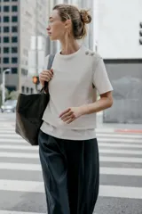 Top de cuello redondo y manga corta con diseño de capas que combina una remera de algodón blanca con un chaleco de punto gris superpuesto. Presenta detalles de botones joya en el hombro.