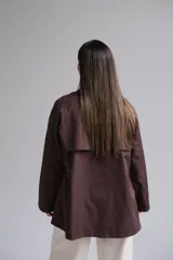 Trench corto color chocolate, con cuello solapa, cierre frontal cruzado con botones y mangas largas.