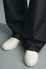 Zapatilla deportiva de estilo retro con diseño de paneles en combinación de colores crema, verde azulado y detalle en rojo en el talón. Presenta suela con volumen y cierre con cordones.