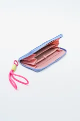 Billetera rectangular con cierre, color celeste pálido, con parche frontal negro que lleva las letras "CNJ" en relieve. Incluye un llavero de muñequera con cordón trenzado en rosa fuerte y verde lima.