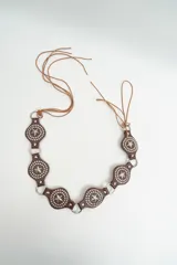 Cinturón negro de estilo western con apliques metálicos circulares y estrellas grabadas, unido por argollas metálicas y terminado con tiras largas de cuero para atar.