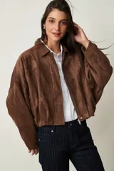 Campera de gamuza marrón, de corte oversize con hombros caídos, cuello camisero, cierre frontal de cremallera y puños y dobladillo elásticos.