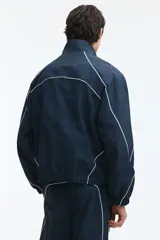 Campera deportiva de nylon en color verde oscuro con estampado a cuadros, cuello elevado, cierre frontal y ribetes blancos en contraste. Cuenta con elástico en puños y bajo, y forro de malla.