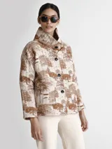 Saco acolchado con estampado toile de jouy en tonos beige y marrón, con cuello alto y cierre frontal con botones negros.