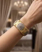 Brazalete ancho de bronce con acabado texturizado dorado, adornado con aplicaciones de circonias formando motivos florales y estelares en tonos plateados.