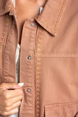 Sobrecamisa de algodón color marrón claro, con cuello camisero y cierre frontal de botones a presión. Presenta detalles de bordado vertical en el frente y en los puños.