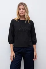 Remera blanca de manga tres cuartos con detalles de bordado calado en el frente y en los hombros, con cuello redondo y puños elásticos.