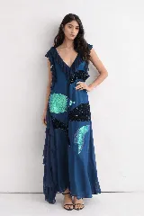 Vestido largo azul de corte fluido con escote en V profundo y volados decorativos en los hombros y laterales. Presenta apliques de lentejuelas en tonos negro y verde iridiscente distribuidos en el frente.