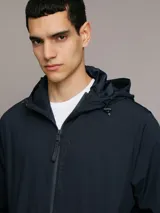 Campera rompeviento Calvin Klein de color azul marino, con cierre frontal de cremallera, capucha ajustable y bolsillos laterales. Presenta un parche con el logo de la marca en la manga y puños elásticos.
