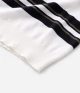 Remera boxy de punto listrado en blanco, negro y verde oliva, con cuello polo y abertura frontal con botones. Posee caída cómoda y textura suave.