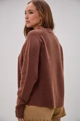 Sweater de tejido de punto color marrón chocolate, con cuello redondo y mangas largas con puños ajustados. Presenta un corte recto y holgado con el ruedo ligeramente asimétrico.