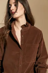 Camisa de pana color crema con cuello camisero con volados, cierre frontal de botones y mangas largas con puños abotonados. Presenta un bolsillo aplicado en el pecho y una silueta relajada.