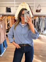 Camisa de corte oversize con estampado de rayas finas verticales en tonos celeste y blanco. Presenta cuello camisero, cierre frontal con botones, bolsillo en el pecho y mangas largas con puños.