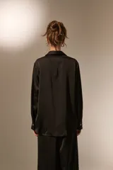 Camisa de poliéster con acabado satinado, de corte holgado, cuello camisero clásico, cierre frontal con botones y mangas largas con puños.