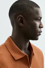 Polo de manga corta color blanco roto, con cuello solapa y cierre frontal de cremallera. Presenta un tejido de piqué estructurado y corte regular fit.