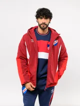 Campera de abrigo corta con capucha, diseño con bloques de color en bordó, rojo y blanco. Presenta cierre frontal, logo de Umbro y escudo del Club Nacional de Football en el pecho.