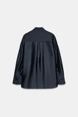Camisa de corte holgado confeccionada en mezcla de lyocell con acabado satinado. Presenta cuello redondo con lazadas integradas, cierre frontal con botones ocultos bajo solapa, bolsillos de plastrón en el frente y mangas largas con puños anchos. El bajo es asimétrico y redondeado.