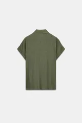 Camisa blanca confeccionada en tejido con lino, con cuello solapa y manga muy corta con terminación en vuelta. Presenta un detalle de nudo en el delantero y cierre frontal con botones metálicos.