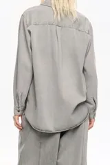 Camisa de manga larga color gris claro con efecto lavado, corte recto y botones frontales marrones. Presenta cuello camisero y pespuntes a contraste.