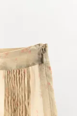 Shorts de tiro medio confeccionados en tejido de organza semitransparente con estampado floral sutil. Presenta diseño con pliegues verticales, aplicaciones bordadas a contraste en el bajo y terminación con puntilla. Cuenta con cierre lateral mediante cremallera oculta.