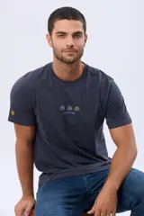 Remera de manga corta color azul oscuro, con cuello redondo y detalle de bordado pequeño en el centro del pecho que representa tres figuras geométricas con forma de árboles y el texto Legacy Brand.