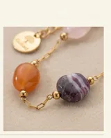 Pulsera de cadena fina con baño de oro, adornada con piedras naturales de diversos colores y formas, incluyendo tonos violeta, blanco y naranja.