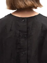 Remera de lino con corte holgado, cuello redondo y mangas cortas. Presenta un diseño minimalista con detalle de botones en la espalda.