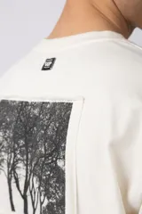 Remera de corte oversize confeccionada en algodón premium de gramaje pesado, color crudo. Presenta un bordado frontal pequeño en el centro del pecho con un diseño de dos árboles unidos por sus raíces y un parche estampado en la espalda con una silueta de mano fusionada con ramas.