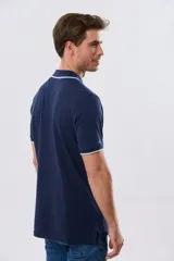 Remera polo de piqué azul marino, con cuello y puños de mangas cortas con ribete blanco en contraste, cierre frontal de dos botones y pequeño logo bordado en el pecho.