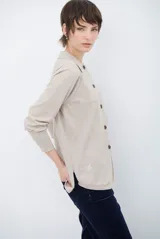 Cardigan de punto color beige, con cuello camisero, cierre frontal de botones y bolsillo aplicado en el pecho. Presenta mangas largas con puños acanalados y un corte recto y holgado.