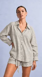 Camisa de manga larga color gris claro, de corte holgado, con cuello clásico, cierre frontal con botones y sutil textura grabada en la tela.