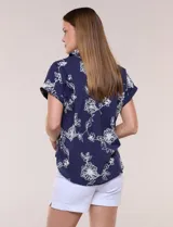 Blusa azul marino de corte amplio en tejido de puro algodón, con cuello camisero abierto en V y detalle de bordado floral en color blanco en toda la superficie. Cuenta con mangas cortas de hombro caído con puño doblado fijo y ruedo curvo con espalda más larga.
