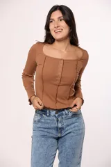 Remera de manga larga en tejido acanalado color marrón, con escote cuadrado y cierre frontal decorativo con botones metálicos. Presenta costuras verticales expuestas en el frente y terminaciones con ondas en los puños.
