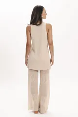 Pantalón de tejido de punto negro, corte ancho y tiro alto, con detalle de encaje calado en la parte inferior. Se lleva debajo de un vestido largo de encaje negro con tirantes finos y botones frontales.