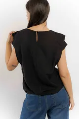 Remera sin mangas de corte holgado, con hombreras marcadas que crean un efecto de manga corta estructurada. Presenta un diseño minimalista con frunces laterales en la cintura y cuello redondo.