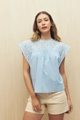 Blusa celeste de manga corta con broderie en el canesú y las mangas. Presenta cuello redondo con terminación de puntilla y recorte fruncido.