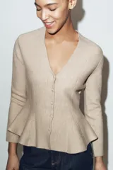 Chaqueta entallada de punto con escote en pico y manga larga. Presenta un diseño con bajo en evasé tipo peplum y cierre frontal con botones forrados a tono.