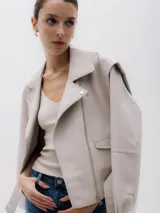 Chaqueta corta estilo biker color beige, confeccionada en piel sintética. Presenta cierre asimétrico frontal, bolsillo con cierre a la vista y bolsillo con solapa, cinturón con hebilla en la cintura.